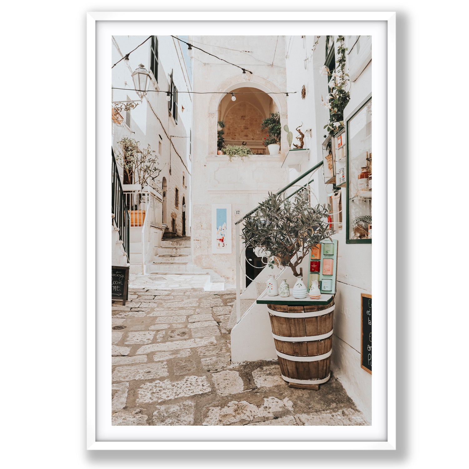 Framed photograph of a quaint outdoor setting in Puglia with a tree in a barrel and stone pavement.