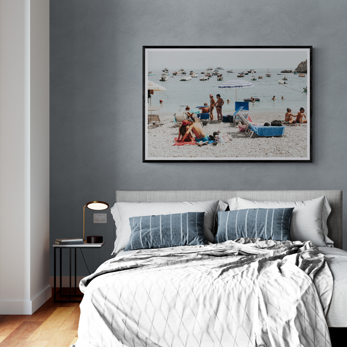 The Kiss Nerano fine art print framed above a bed against a blue-grey wall