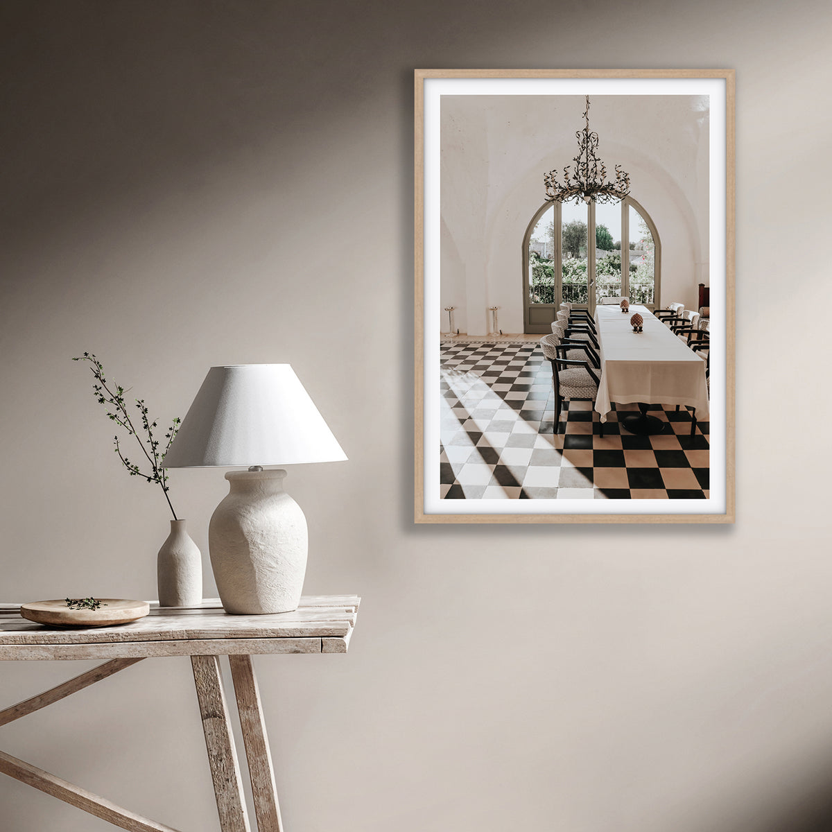 Sunbeam Feast Puglia fine art print in a natural oak frame styled on a warm beige wall beside a white lamp