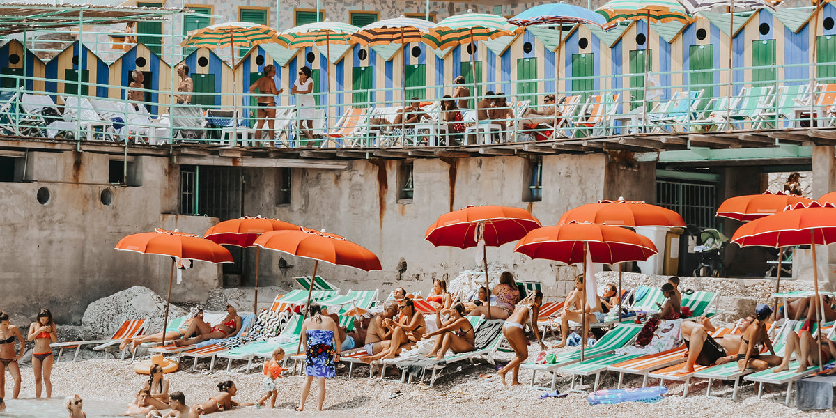 Orange umbrellas and sunbathers below a striped beach club on Capri