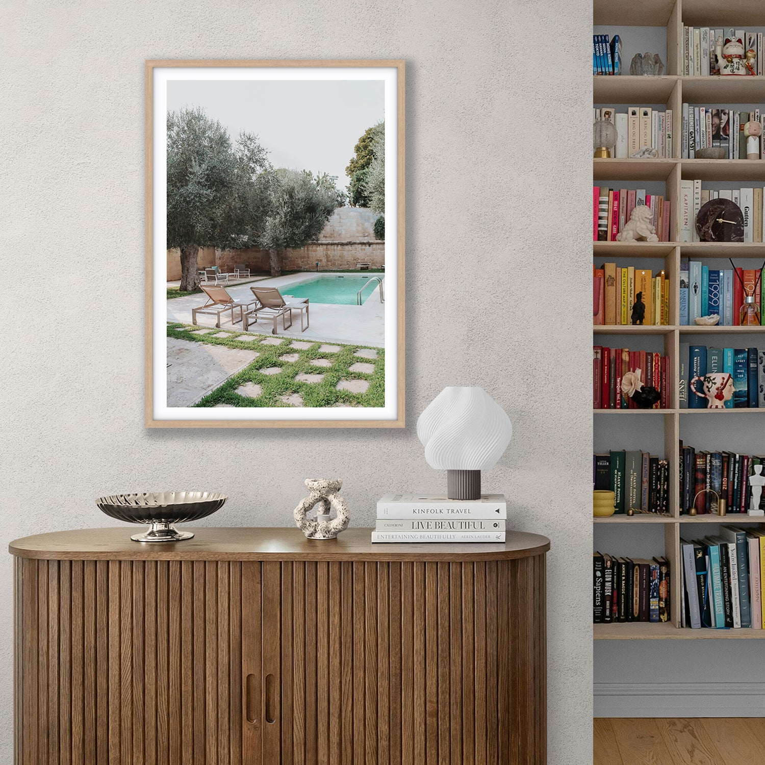 Framed artwork of a backyard scene on a wall above a wooden console table with decor items.