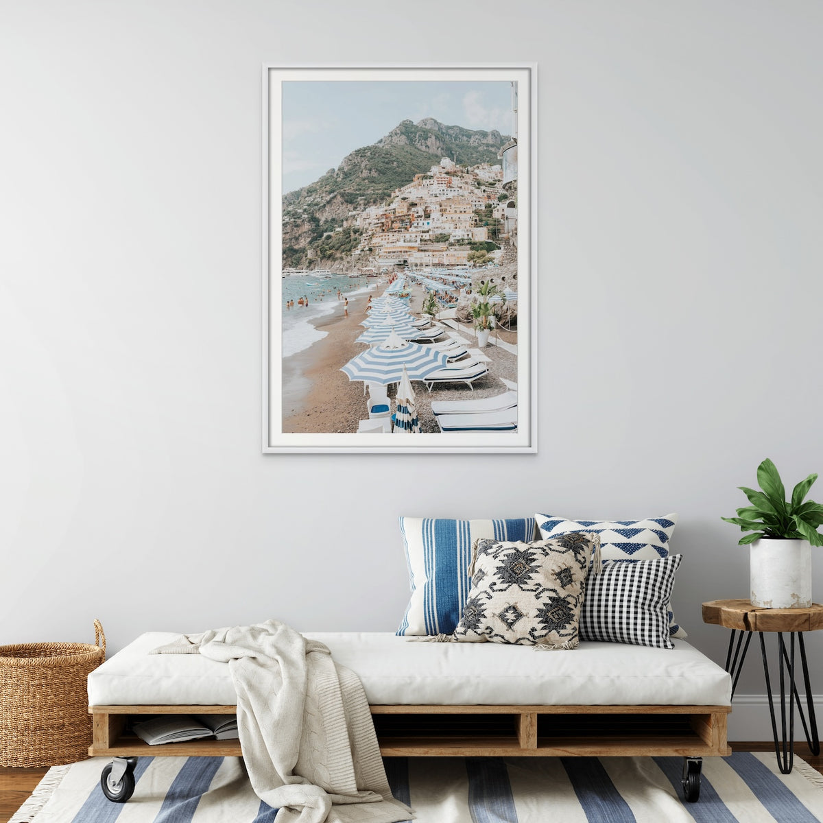 The Cliffside Village, a Positano fine art print in a white frame above a daybed with blue striped and patterned cushions