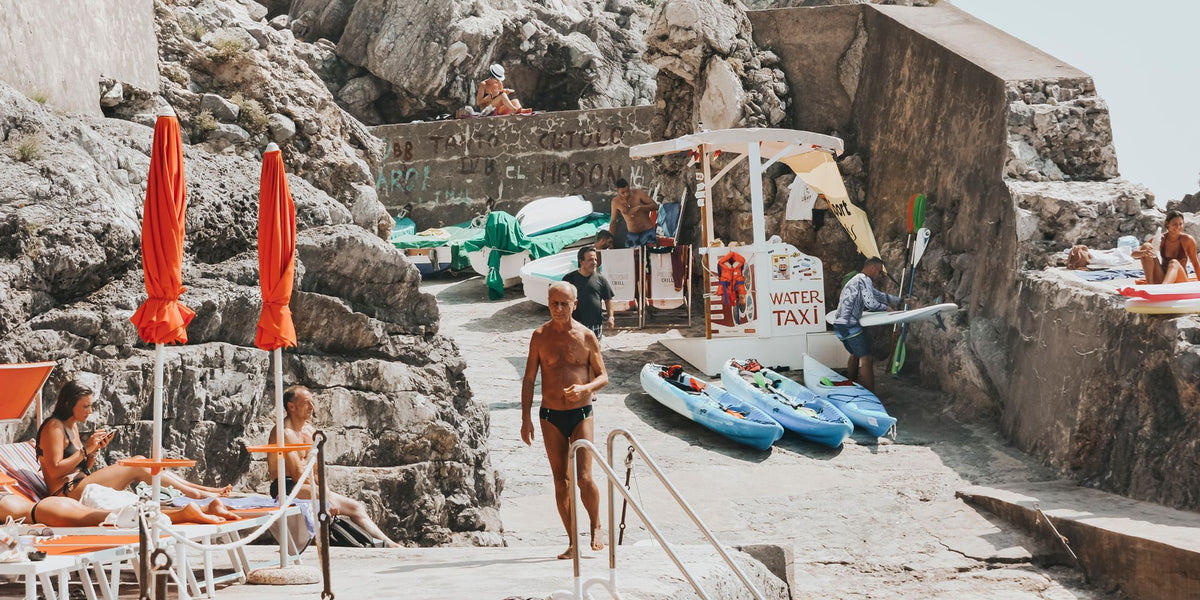An older local in black swimmers walking across the rocks in Praiano
