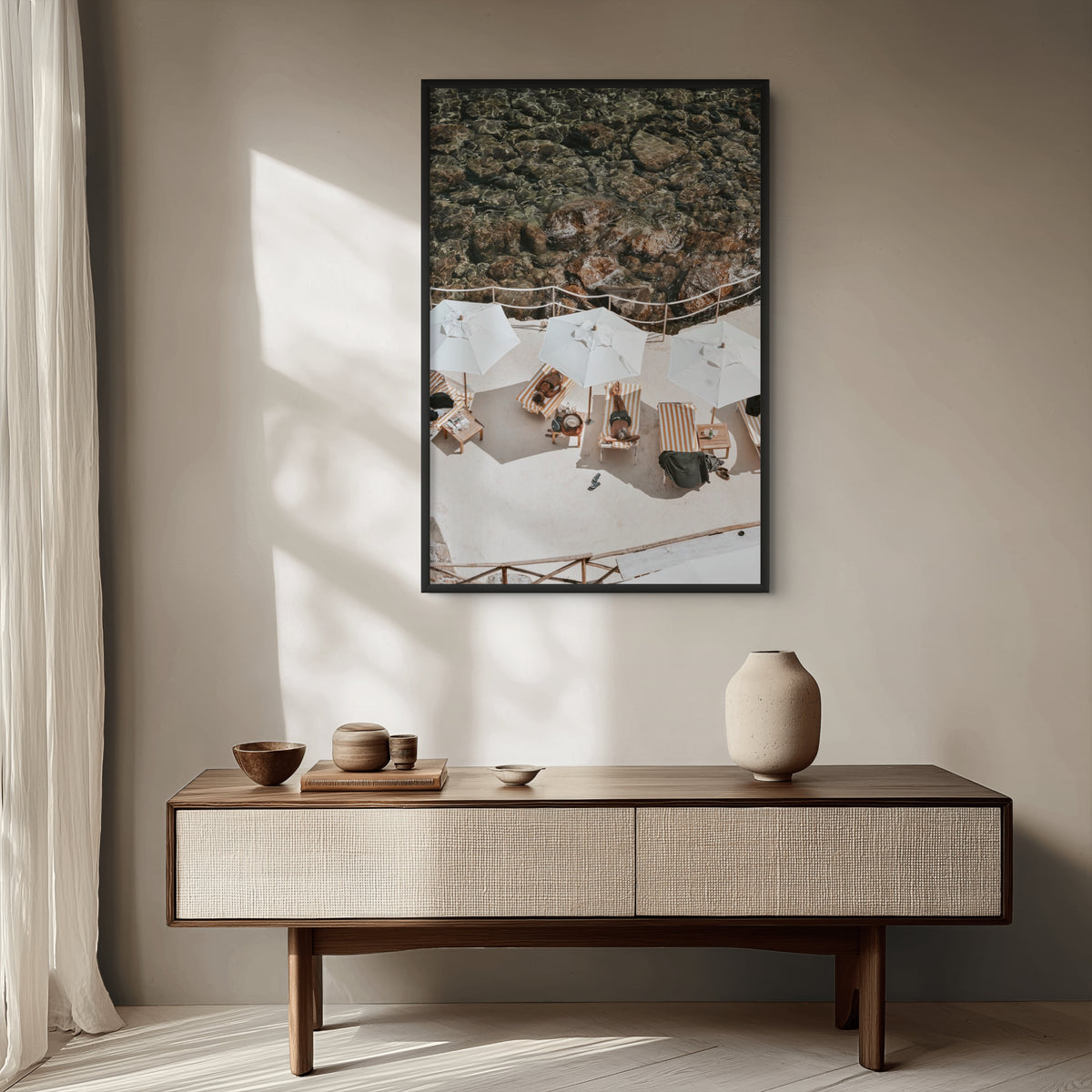 Coastal wall art print of a striped Italian beach club from above, framed in black and styled above a walnut console in a sunlit living room