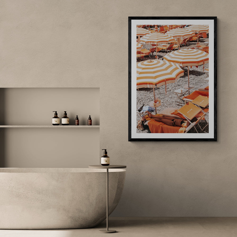 Beach Mode Positano, orange striped umbrellas, loungers and sunbather on pebbles, framed print styled in a room view 2