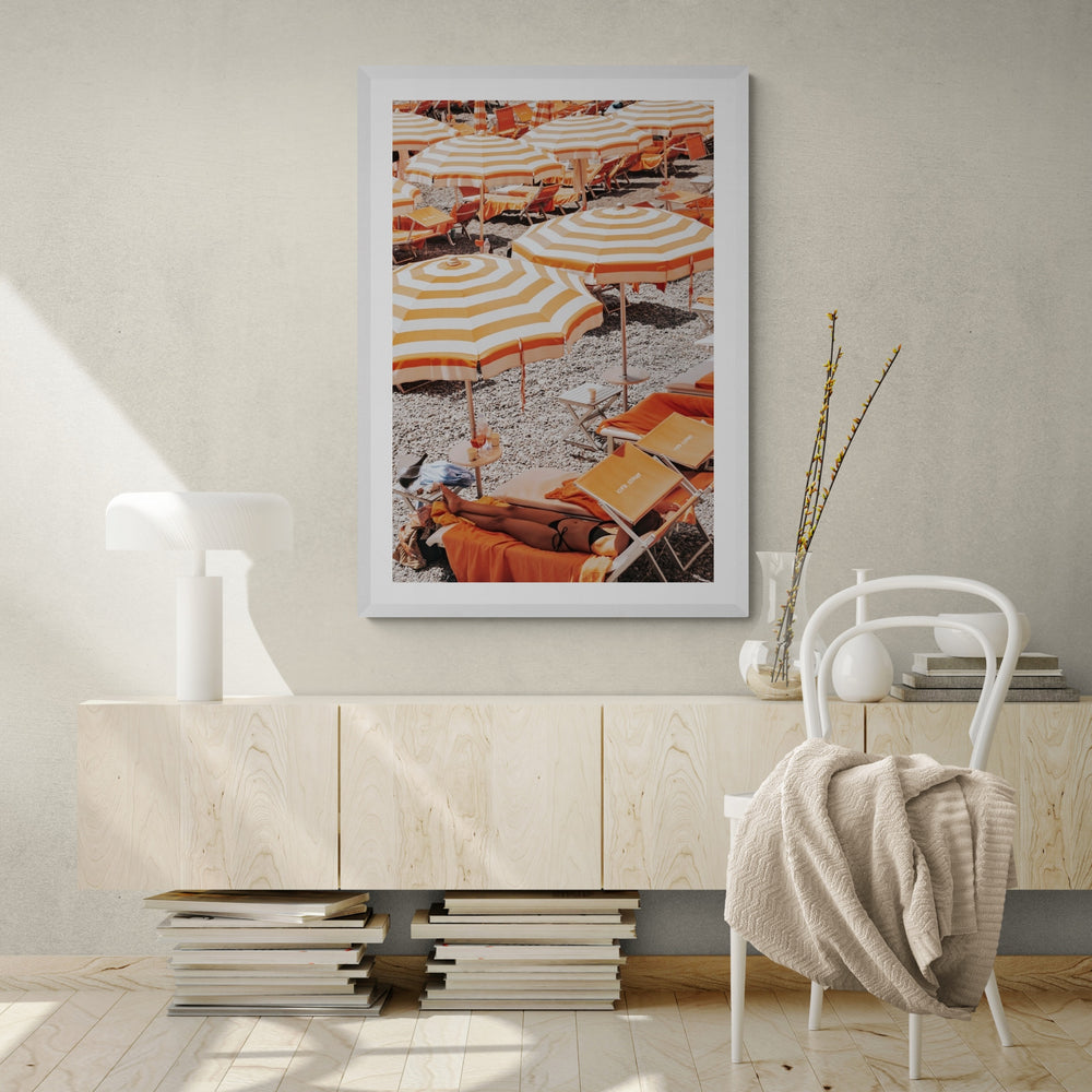 Beach Mode Positano, orange striped umbrellas, loungers and sunbather on pebbles, framed print styled in a room view 3