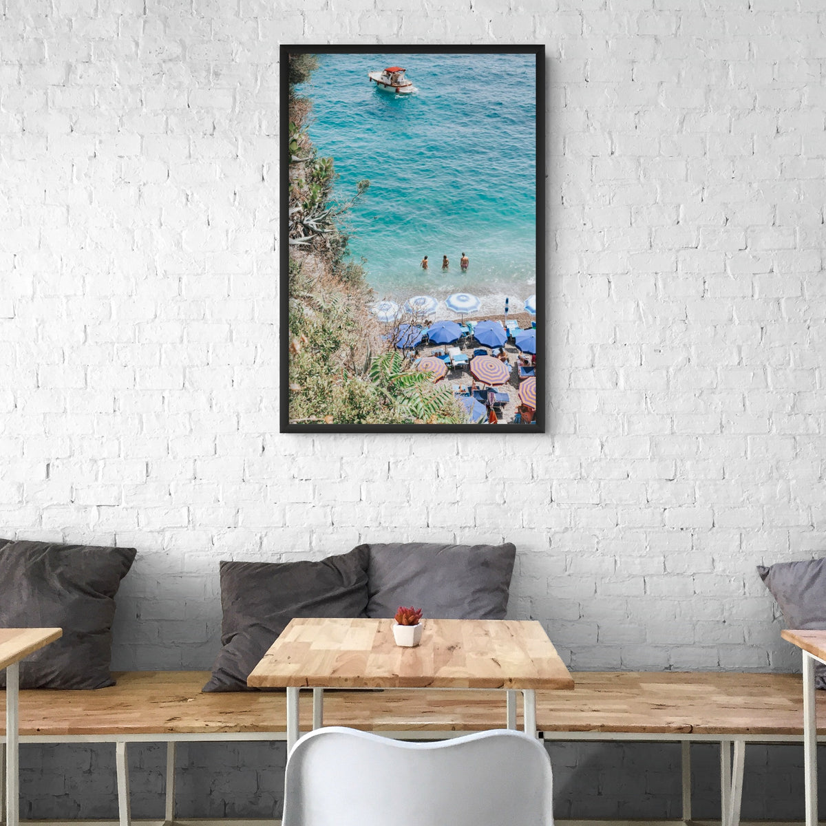 Vitamin Sea Positano, turquoise shallows, swimmers and striped umbrellas framed by greenery, framed print styled in a room